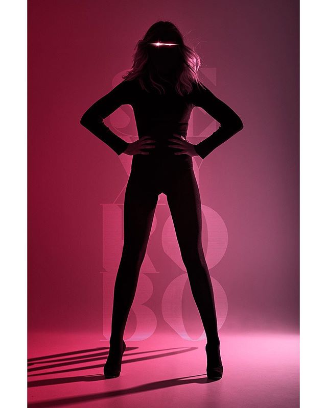 A confident woman poses in silhouette against a red backdrop, embodying strength and style.
