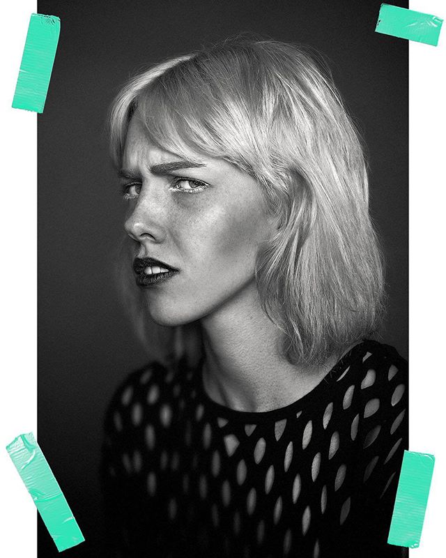 A striking black and white portrait of a blonde woman with an intense expression, in a studio setting.