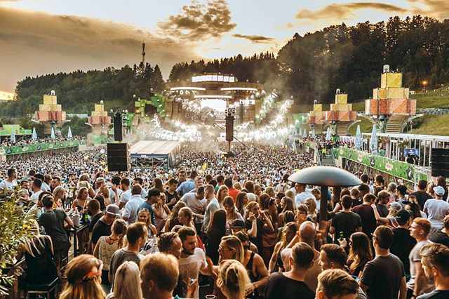 A large crowd of people enjoying an outdoor music festival at sunset, creating a lively and energetic scene.