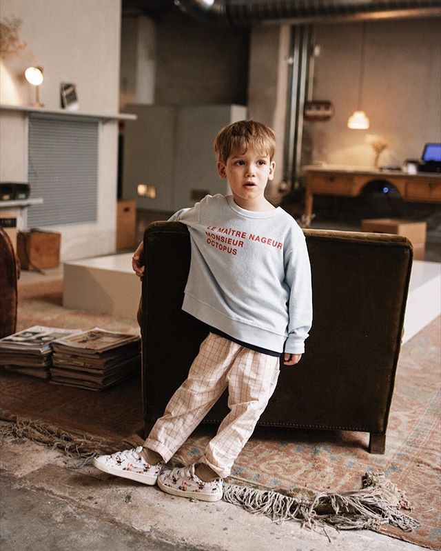 A young boy models in a casual outfit inside a vintage-style room, perfect for showcasing youth fashion.
