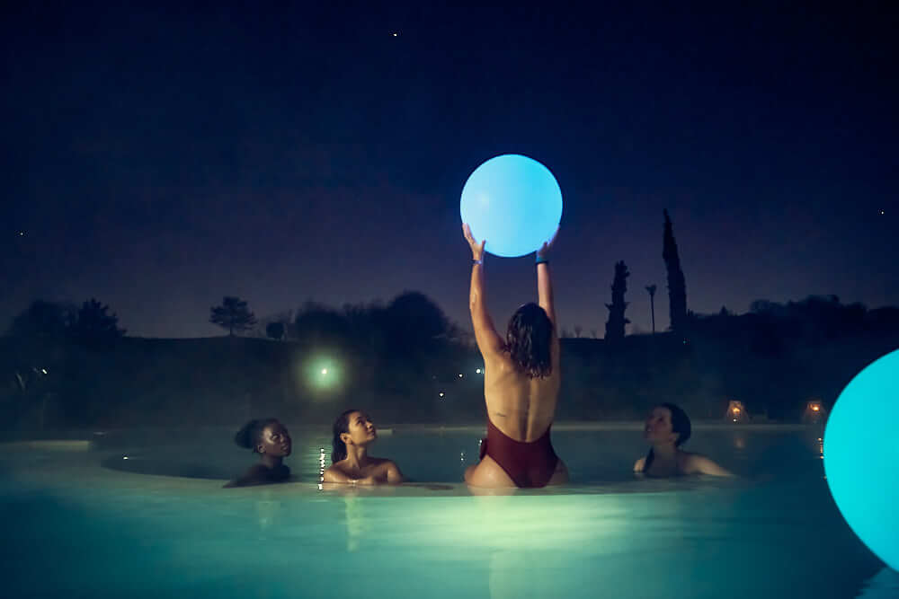 Four women enjoy a nighttime spa with glowing orbs, creating a tranquil and relaxing scene.