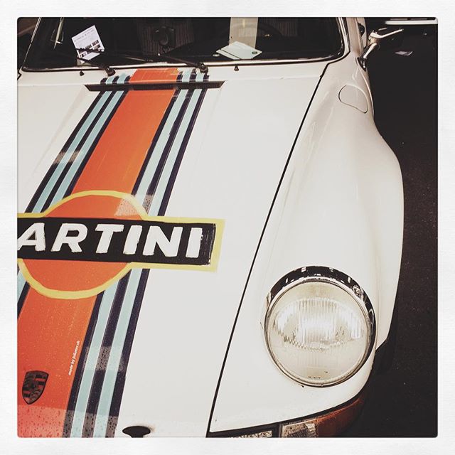 A white Porsche with Martini racing stripes, showcasing vintage automotive design.