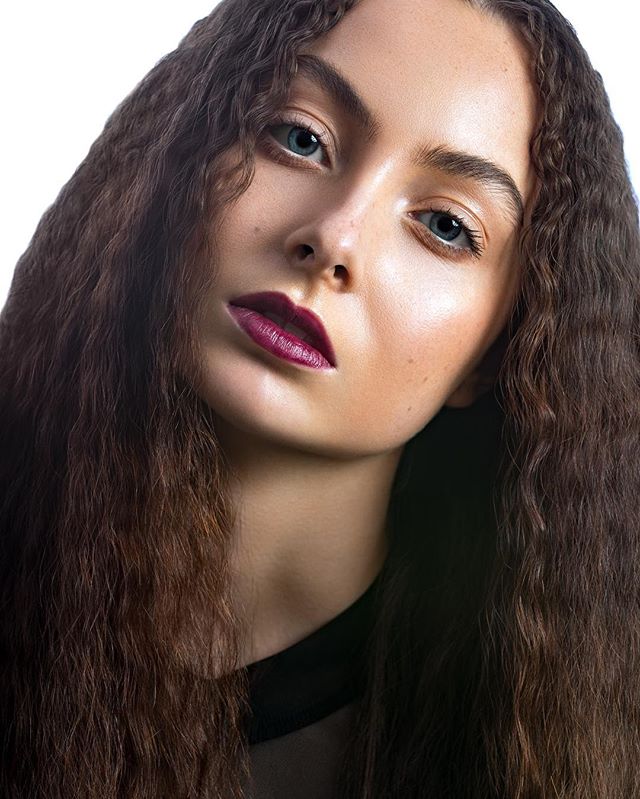 Portrait of a brunette woman with long wavy hair, wearing dark lipstick in a studio setting.