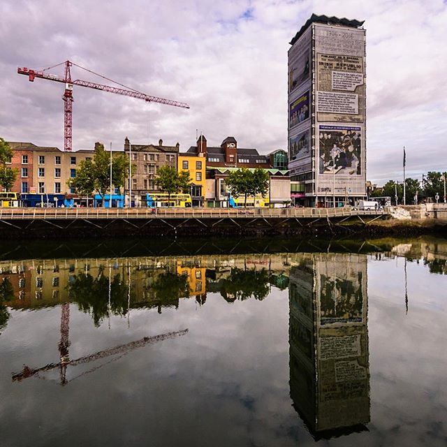 Cityscape featuring a building and a crane reflected in the water, creating a tranquil urban scene.