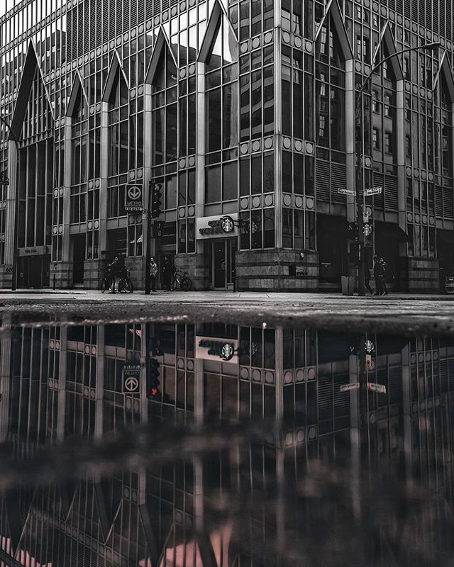 A monochrome reflection shows a Starbucks on a city street with people and modern architecture.