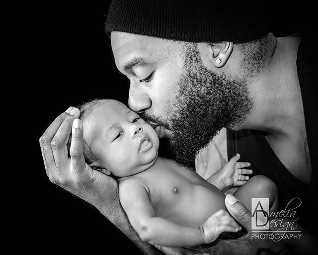 A loving father gently cradles and kisses his newborn baby in a tender, black and white portrait.