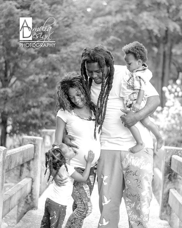 A family poses together on a bridge in a loving black and white portrait. A pregnant woman is surrounded by her family.
