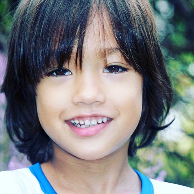 A young boy smiles brightly in a close-up outdoor portrait.