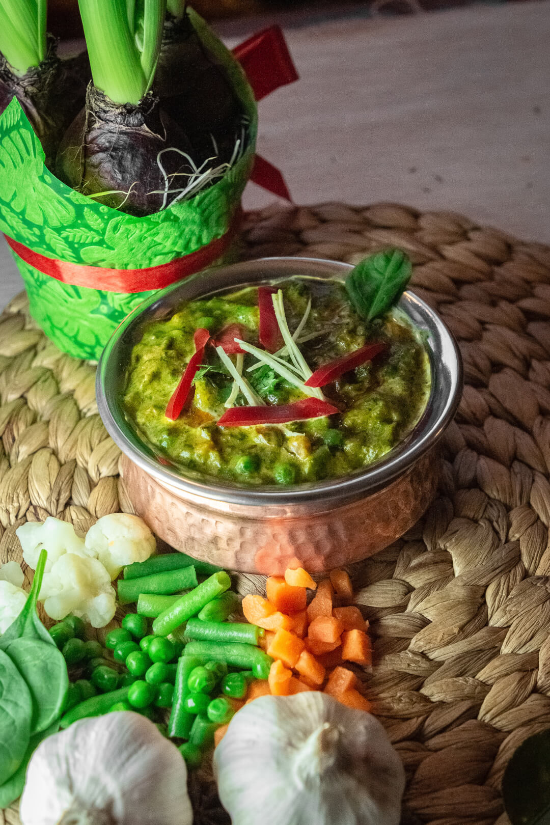 Close-up of saag paneer, an Indian spinach dish, served with vegetables on a woven mat.