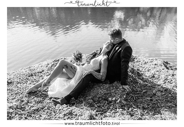 A bride and groom share an intimate moment by the lake, captured in a timeless black and white portrait.