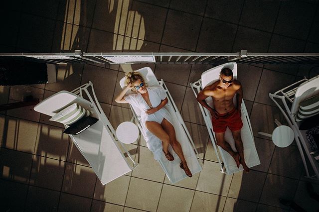 Aerial view of a woman and a man relaxing on lounge chairs in a rooftop pool area.