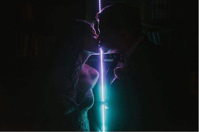 A bride and groom share a romantic kiss, backlit by a vibrant LED light, creating a dreamy and intimate wedding moment.