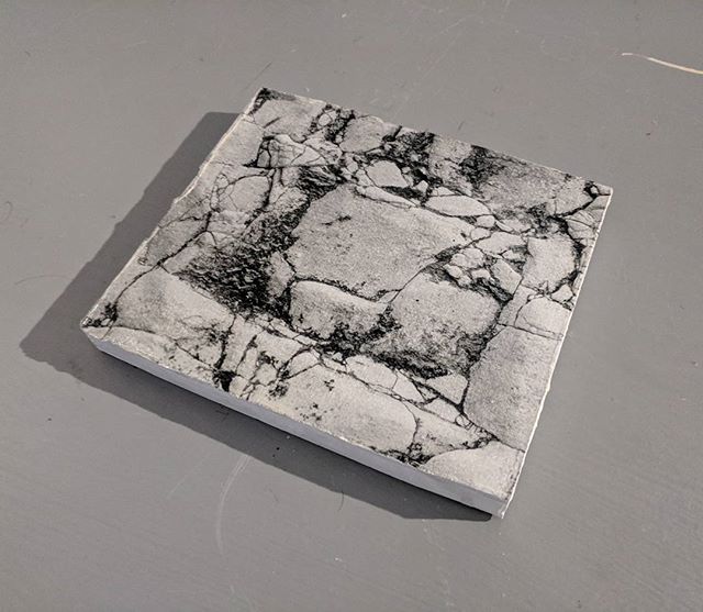 A square stone tile with a natural, cracked pattern sits on a gray surface, ideal for decorative or design projects.