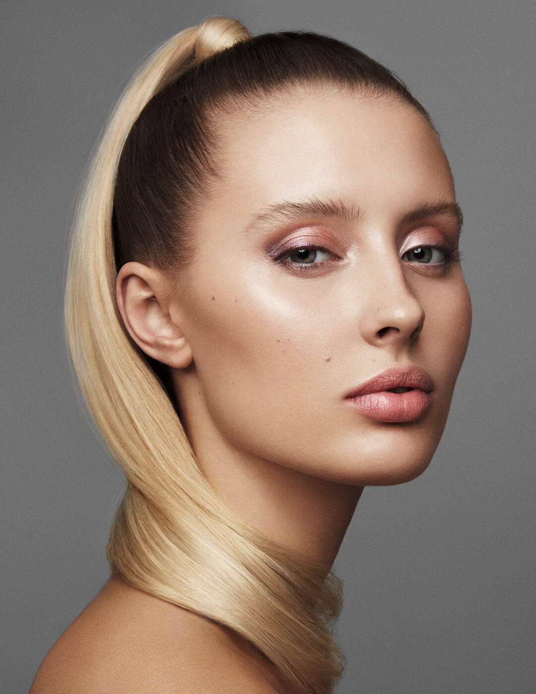 Elegant blonde woman with a ponytail poses in a beauty portrait with soft, dreamy makeup and a modern editorial style.