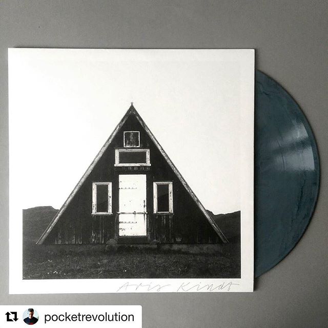 A vinyl record displays a black and white cover with a striking image of a triangular house.