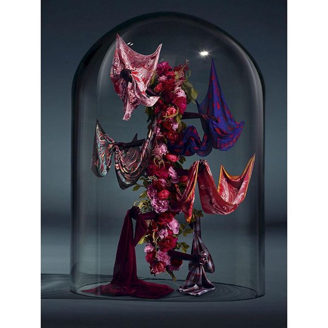 An artistic still life under glass featuring colorful scarves intertwined with flowers. Concept for high fashion editorial or advertisement.