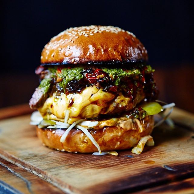 A delicious burger with cheese, toppings, and a sesame seed bun, presented on a wooden board for food blog or menu inspiration.