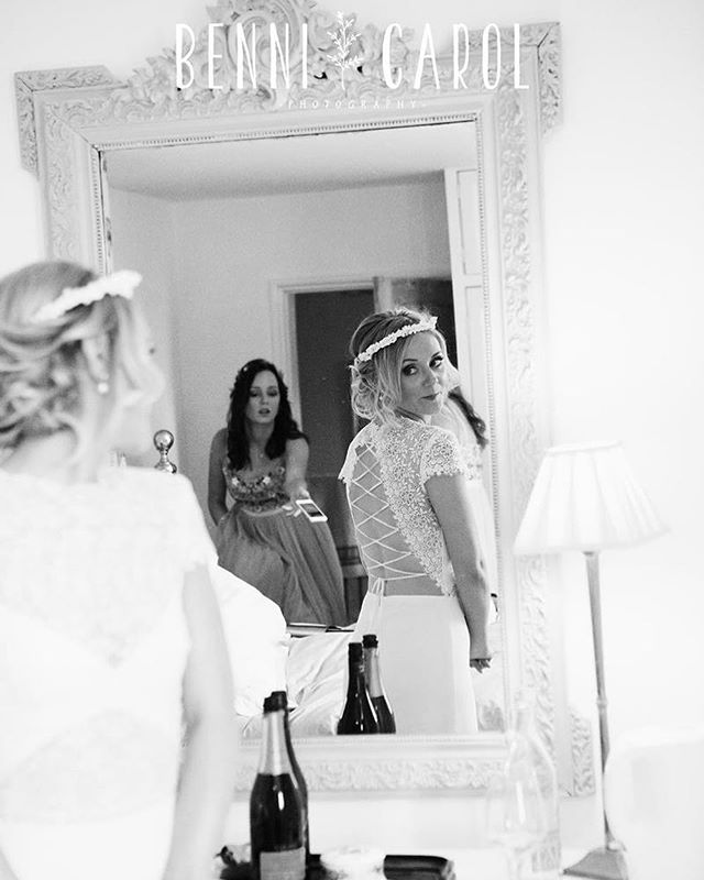 A bride admires herself in the mirror while a bridesmaid looks on in this black and white wedding day photo.
