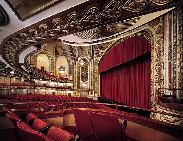 Interior of an ornate theater with red curtains and seating, showcasing classic architecture and elegant design.