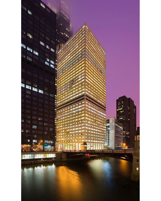 A stunning view of Chicago's illuminated skyscrapers and a river at night under a purple sky.