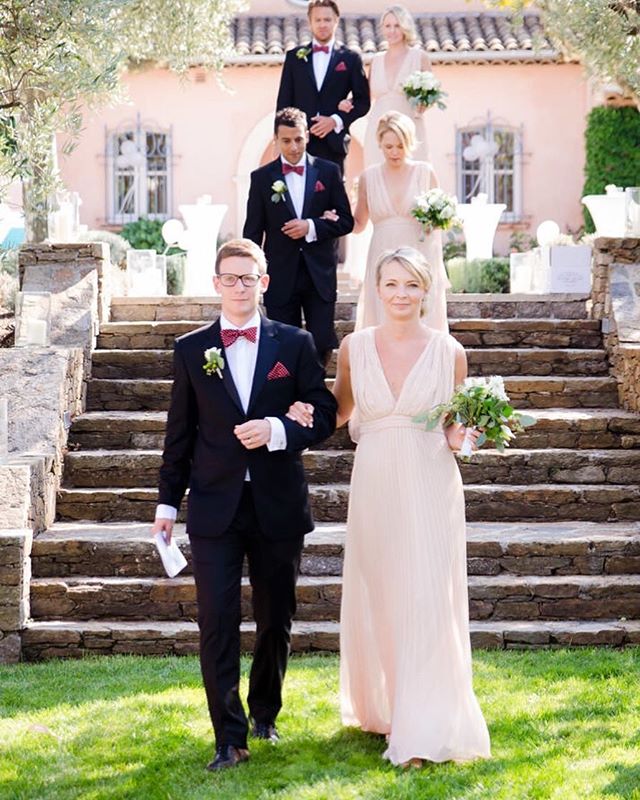 A wedding party, including the bride and groom, descends the stairs at an outdoor venue.