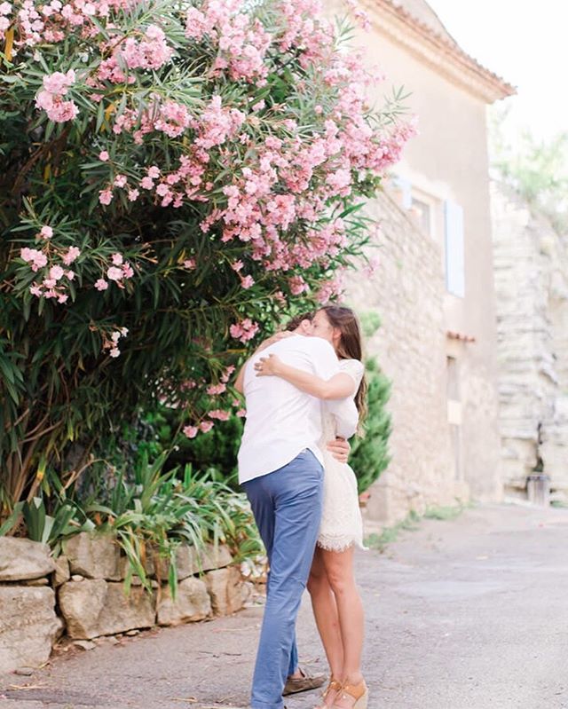 A couple embraces beneath a blooming pink tree on a charming street in Europe.