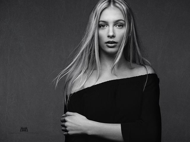 A striking black and white portrait of a blonde woman in a studio setting.
