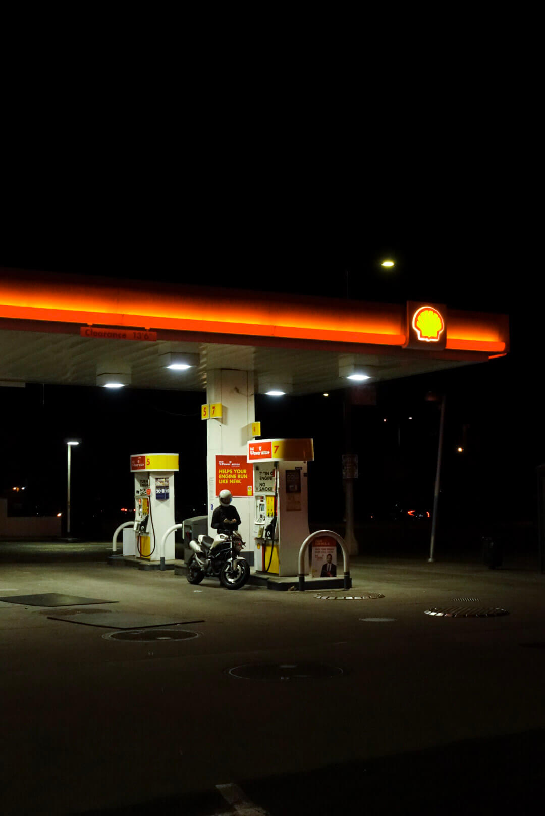 A motorcyclist fuels up at a Shell gas station under the bright glow of the overhead lights at night.