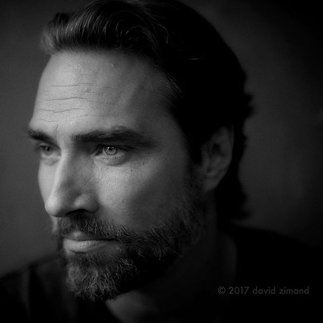 A black and white portrait of a serious man with a beard, gazing off to the side.