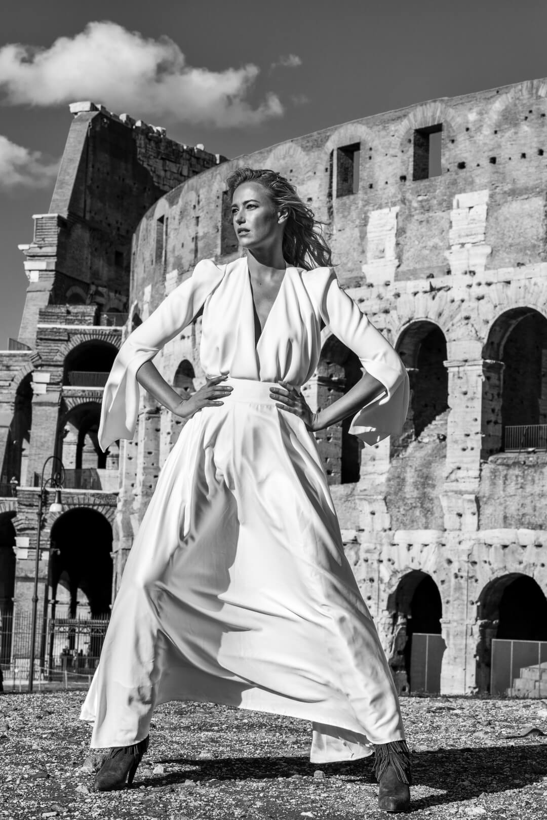 A stylish woman in a white dress poses confidently in front of the Colosseum.
