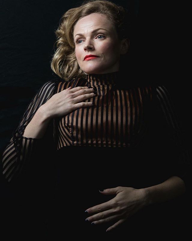 Elegant portrait of a woman in a striped top against a dark background.