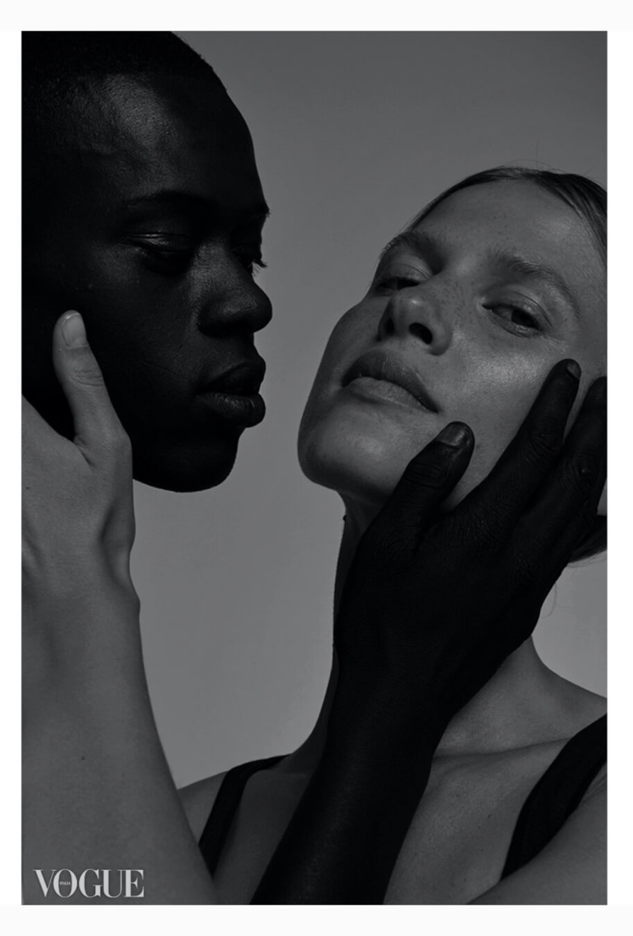 A striking black and white image featuring an interracial couple in a close, intimate pose for a skincare or fashion editorial.