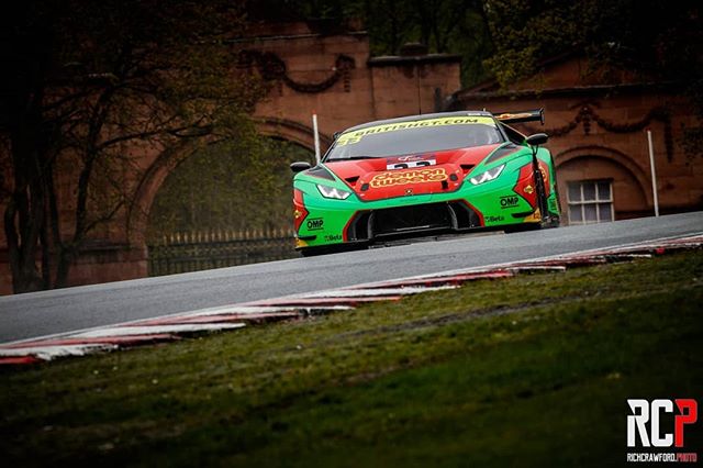 A green and red Lamborghini race car speeds along a racetrack during a motorsport event.