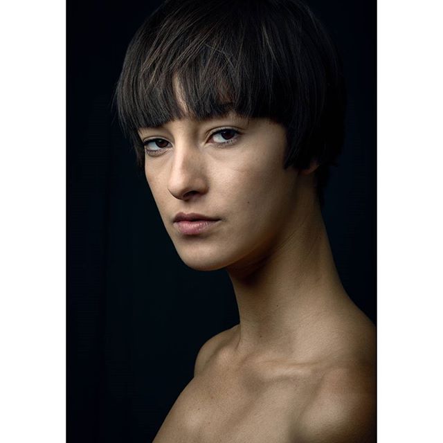 Striking portrait of a young woman with a short haircut, posing against a dark background.