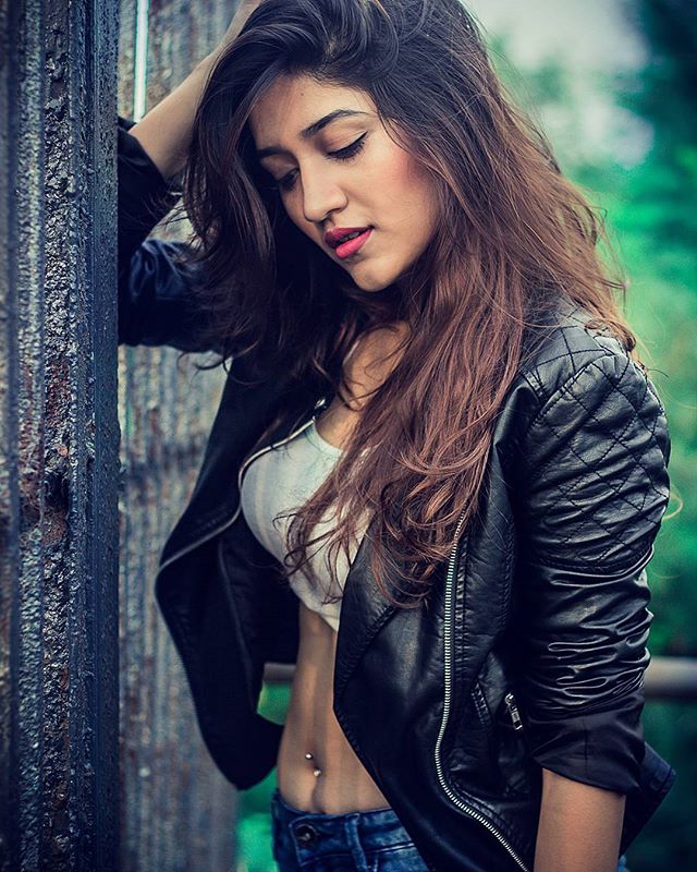 A woman poses in a leather jacket showing her midriff with a belly piercing.