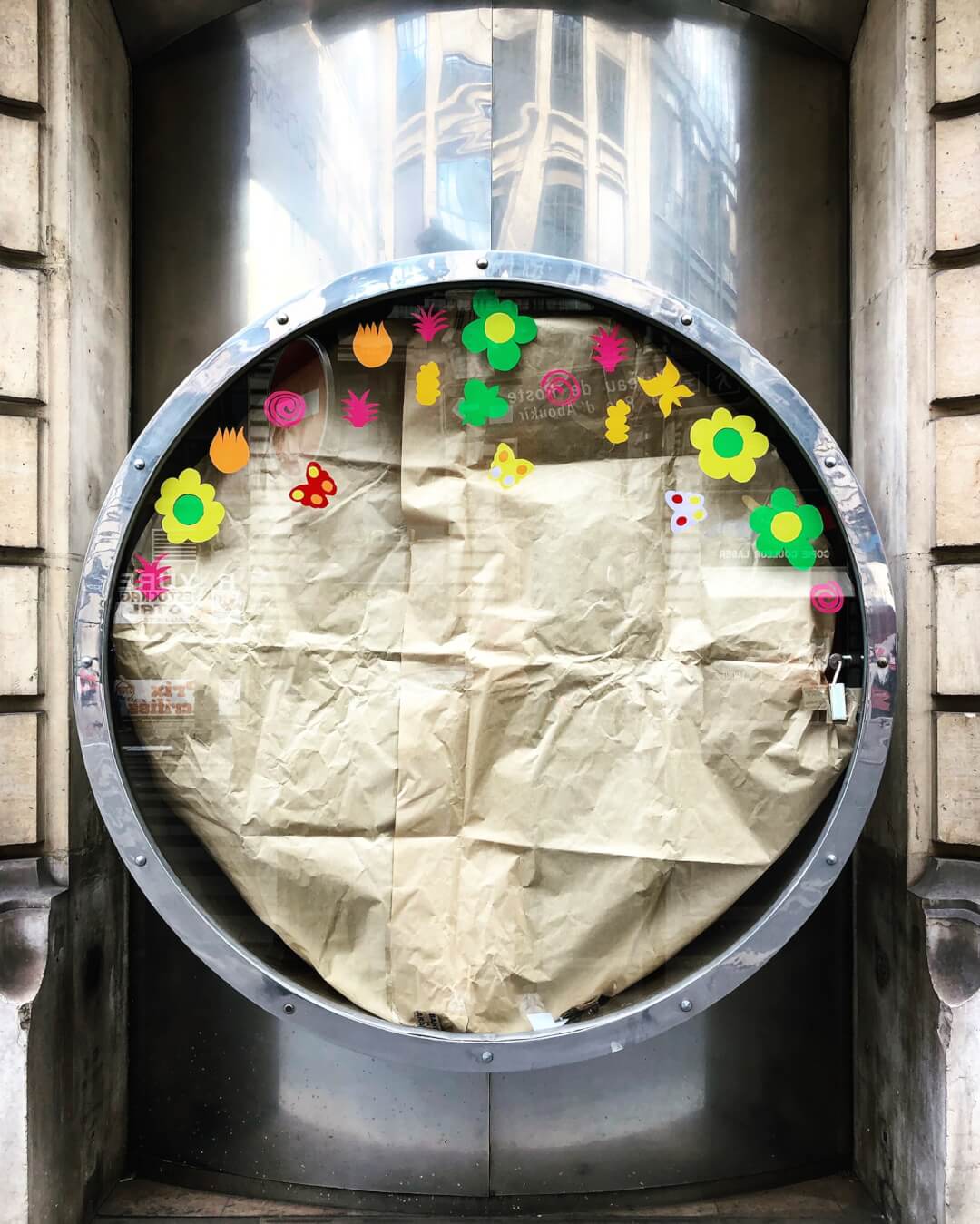 A round shop window display featuring brown paper and colorful flower and butterfly decorations.