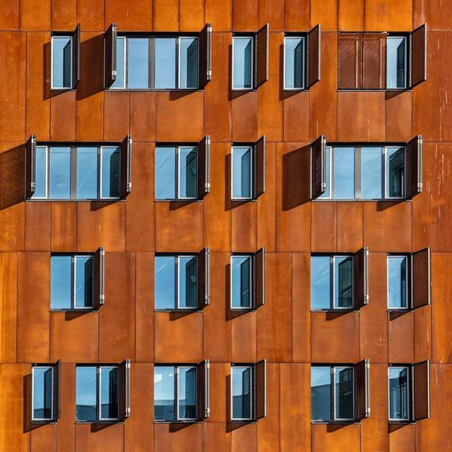 A building facade with a geometric pattern of open windows and a warm, rust-colored exterior.