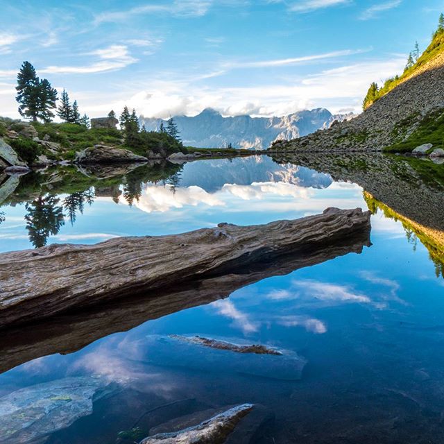 A scenic mountain lake reflects the sky and a fallen log in its clear water. Perfect for nature and travel themes.