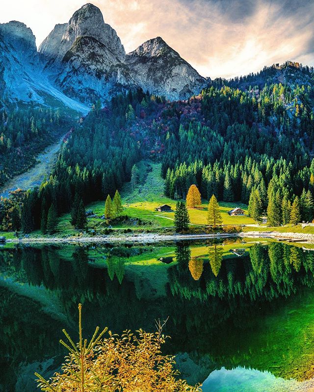 A scenic landscape features mountains, a lake reflecting trees, and cabins nestled in the forest.