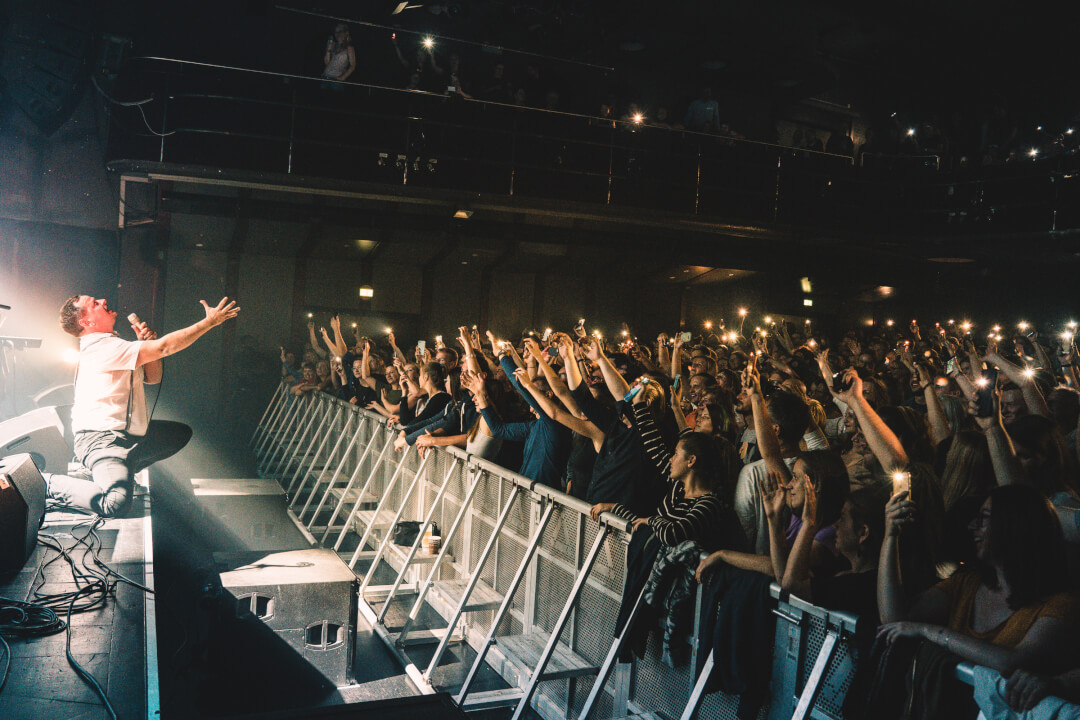 A singer performs on stage to an excited crowd holding up phones at a concert.