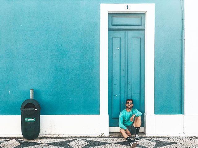 A man sitting by a blue door on a patterned sidewalk adds style to an urban setting.