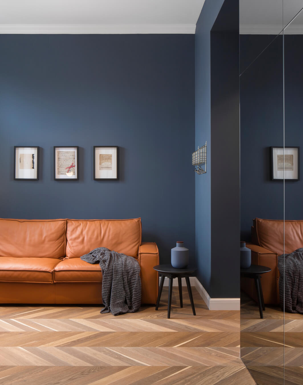 A stylish living room features a brown leather sofa, table, and dark blue walls, creating a calm and inviting space.