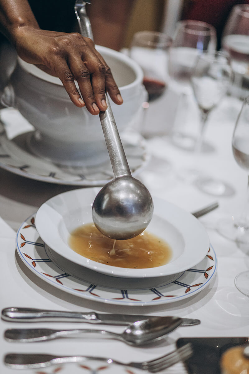 A server pours soup into a bowl on an elegant table setting.