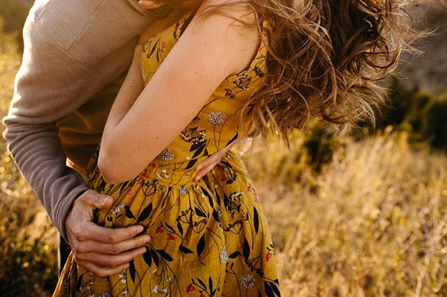 A couple embraces in a sunlit field, showcasing their tender and intimate connection.