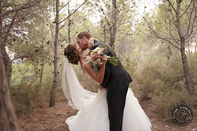 A bride and groom share a kiss in a romantic forest setting on their wedding day.