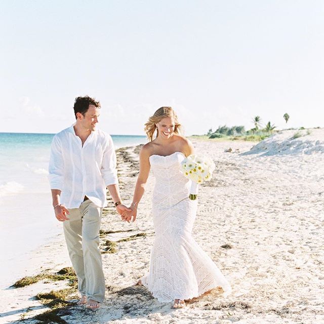 A bride and groom holding hands, walking along a sandy beach, in a romantic, natural setting.