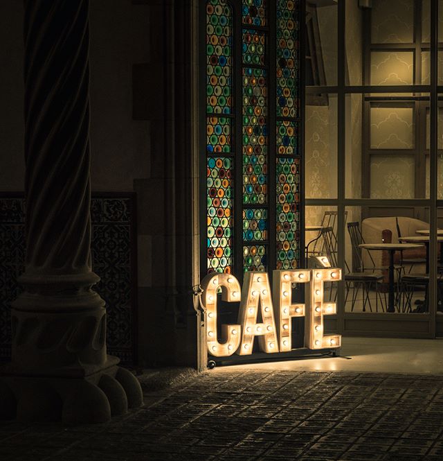 An illuminated 'CAFE' sign stands outside a charming cafe with stained-glass windows at night.