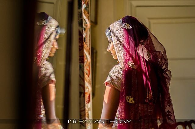 A beautiful Indian bride gazes dreamily at her reflection in a soft light.
