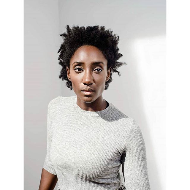 A serious african american woman poses in front of a white wall in a studio.