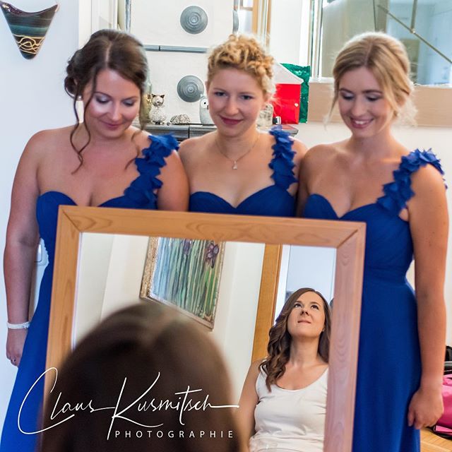 Three bridesmaids in blue dresses look at the bride's reflection in a mirror as she prepares for her wedding.